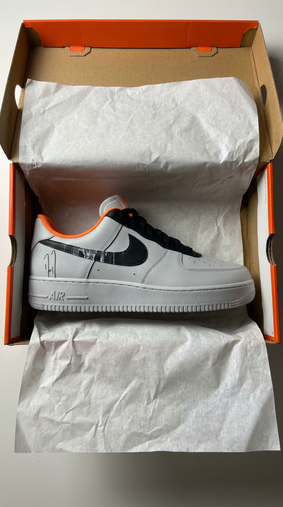 Grey Air Force 1 with a black swoosh resting in an orange Nike box