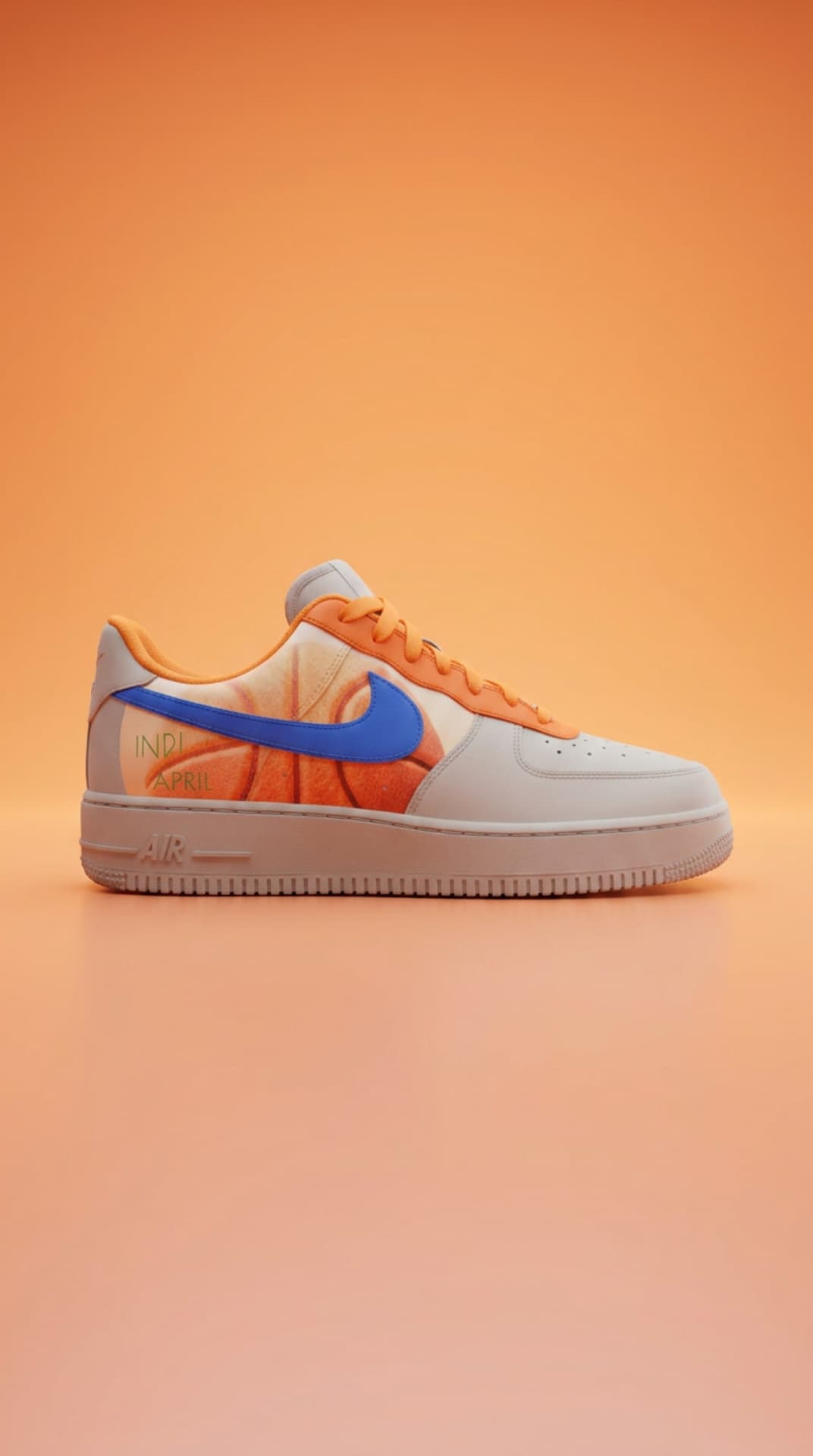 Grey and cream Air Force 1 with a basketball print panel and blue swoosh on a warm orange studio backdrop