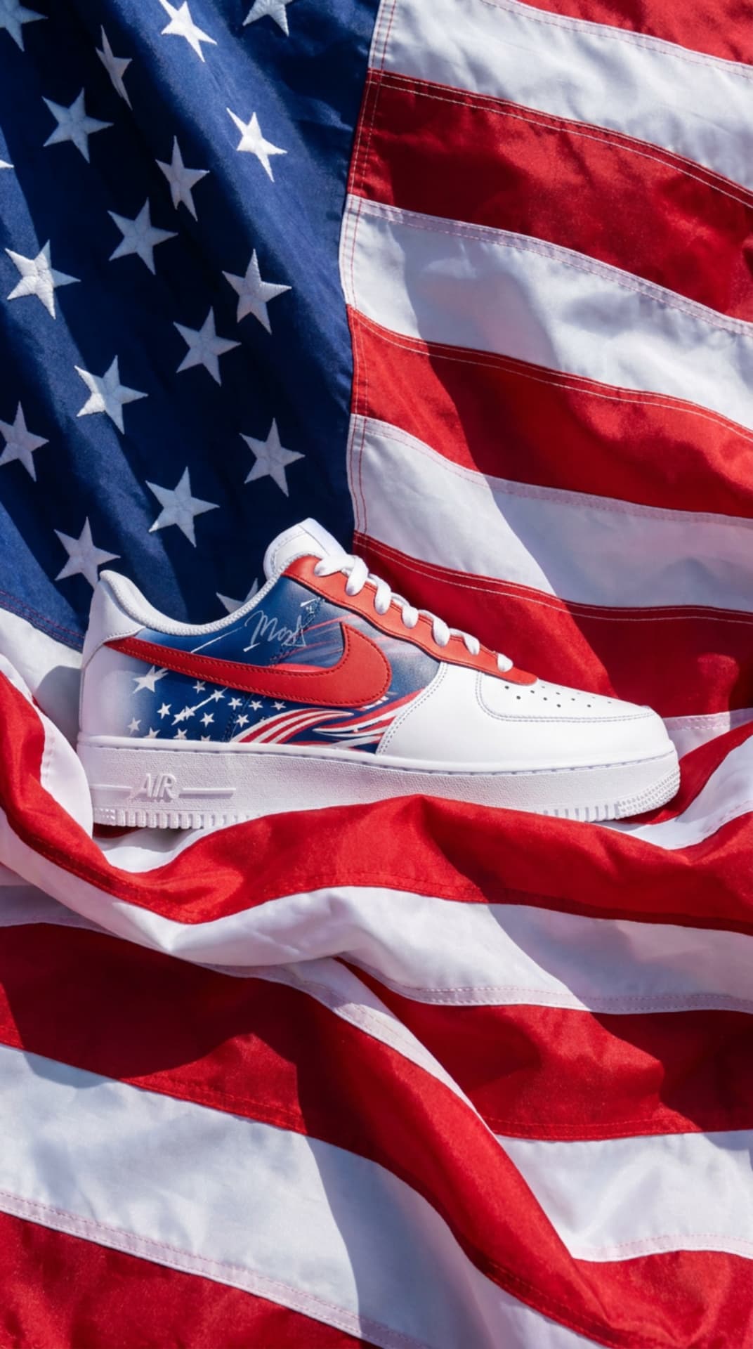 White Air Force 1 with a stars and stripes panel and red swoosh resting on an American flag