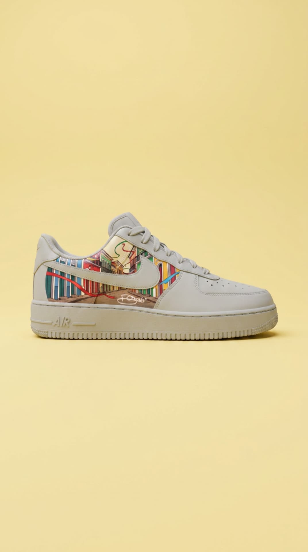 Bone-grey Air Force 1 with a colorful streetscape panel against a soft yellow backdrop