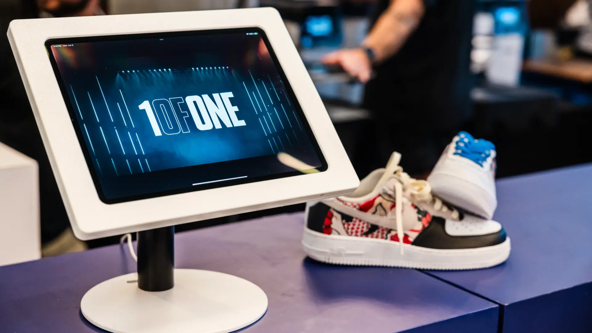 A 1ofONE branded iPad kiosk beside a finished custom Air Force 1 on a blue counter
