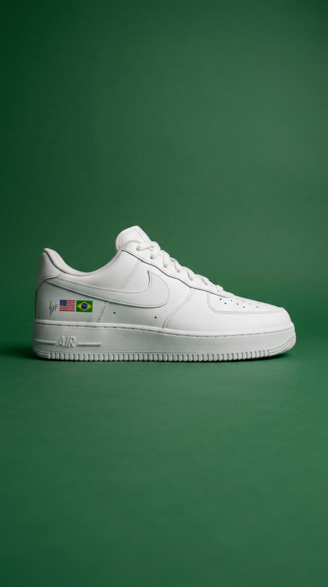 All-white Air Force 1 with USA and Brazil flag decals against a deep green studio backdrop
