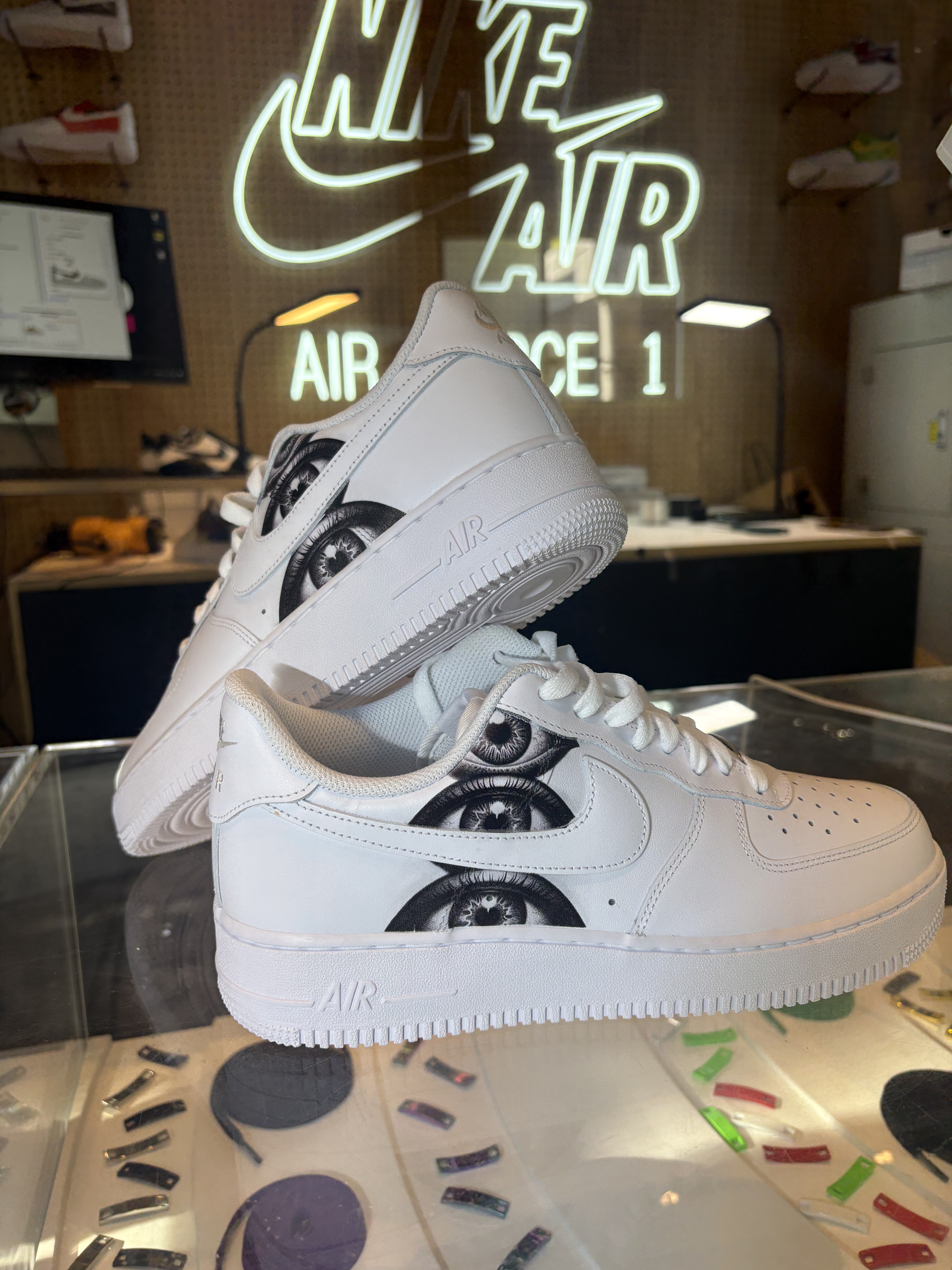 White Air Force 1s printed with black and white eye artwork on a glass display case