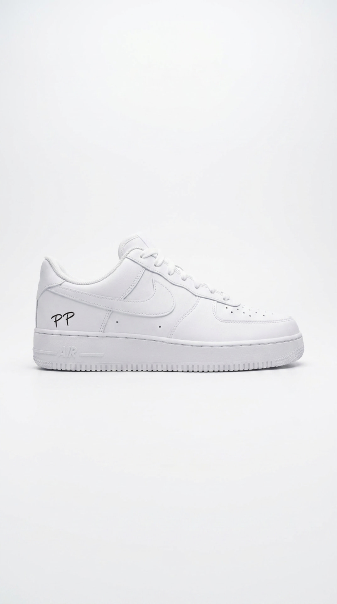 All-white Air Force 1 with a hand-drawn PP script on the heel panel against a bright white backdrop