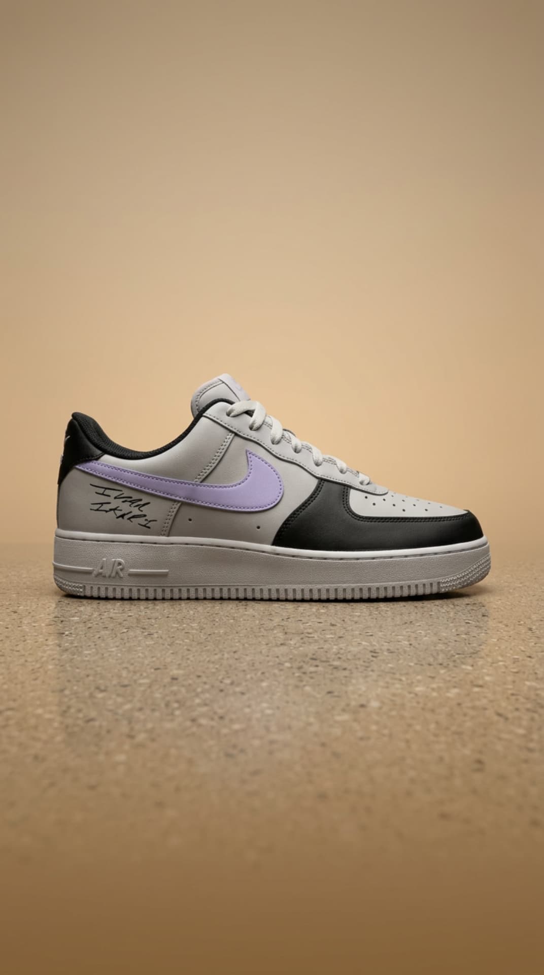 Grey and black Air Force 1 with a lavender swoosh and handwritten signature on a warm sand backdrop
