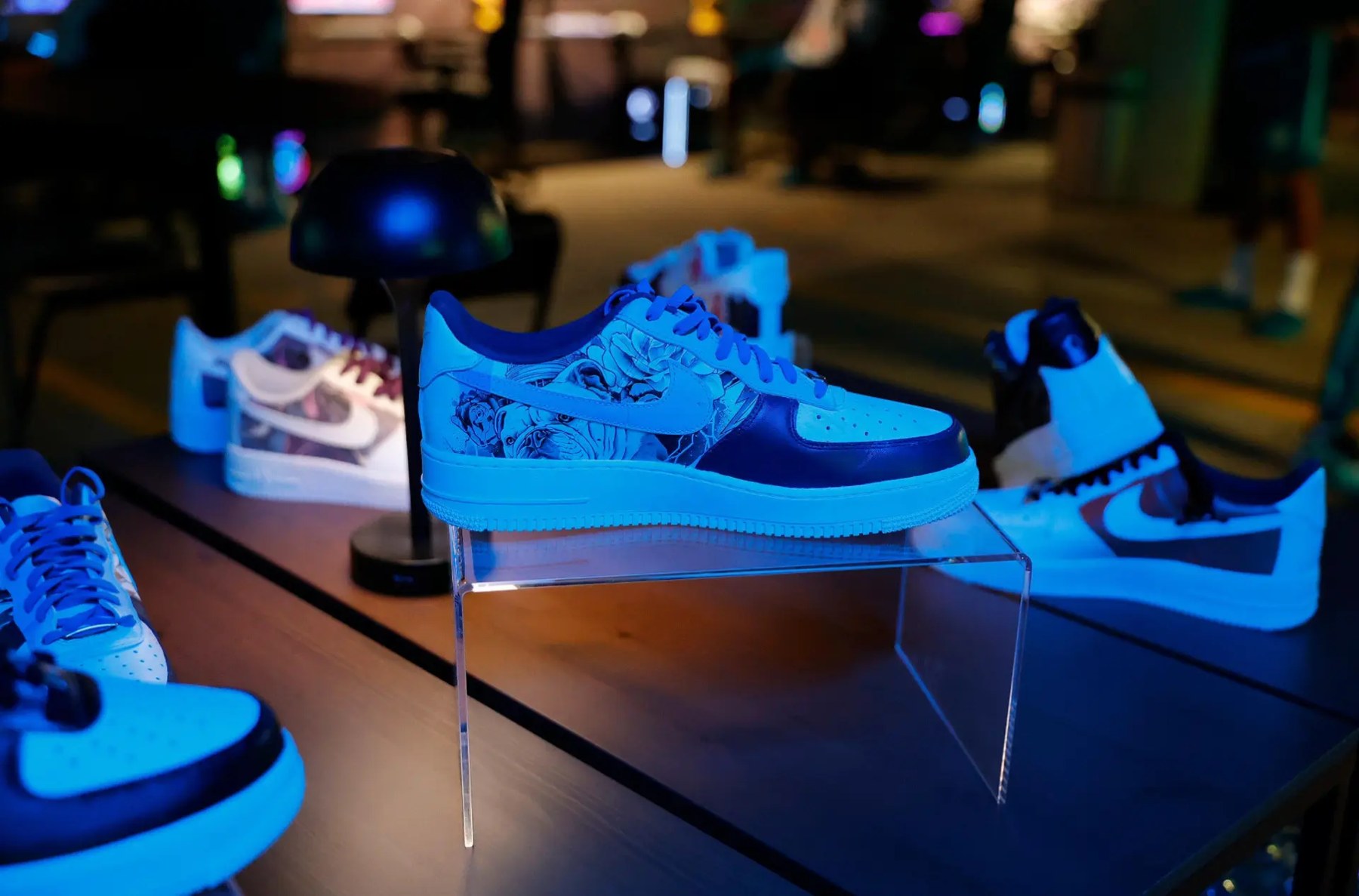 Custom Air Force 1s lined up on a display table under blue event lighting