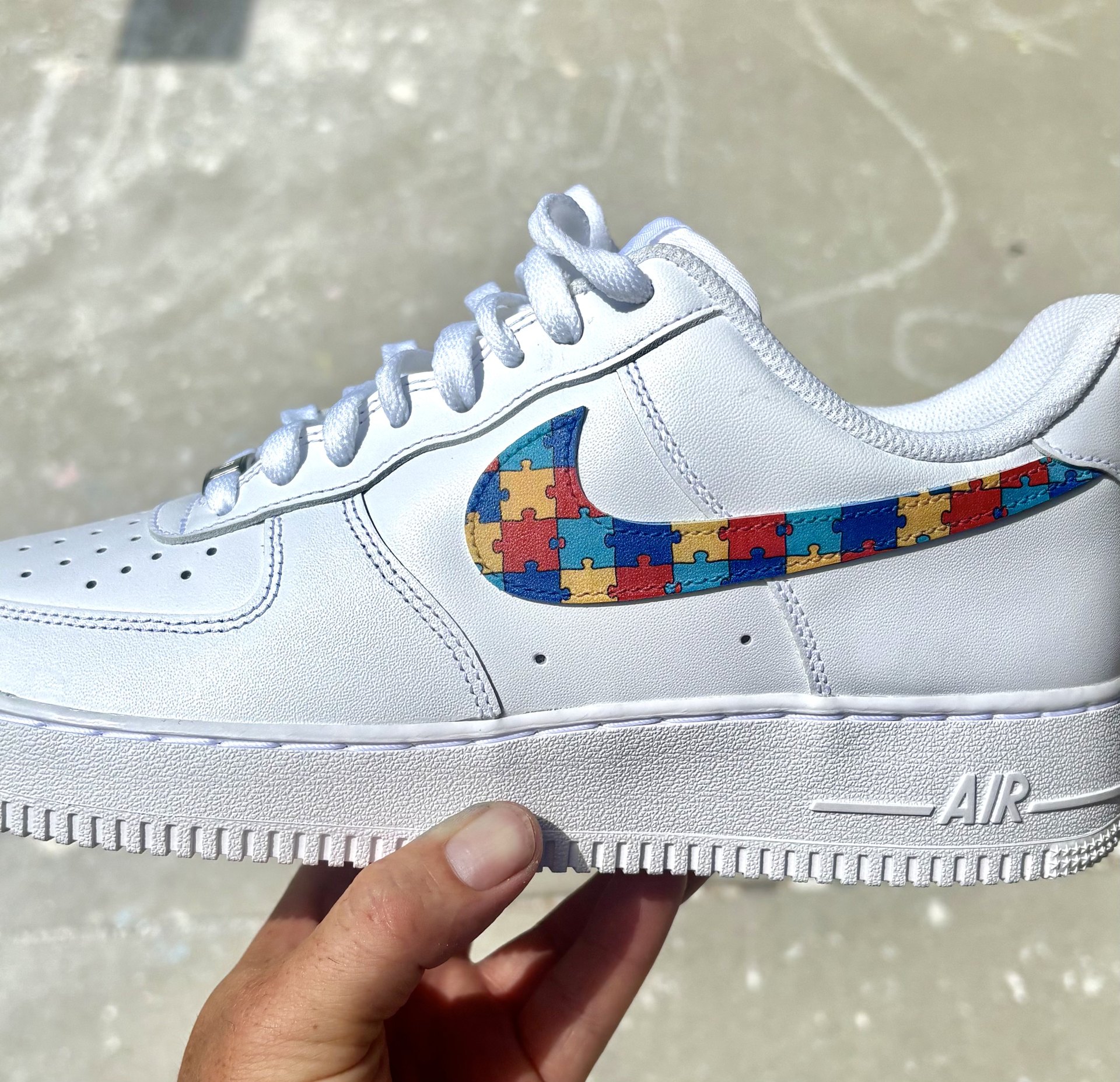 White Air Force 1 held up in the sunlight with a multicolour puzzle-piece printed swoosh